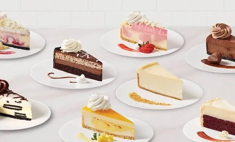 Assorted cheesecake slices on white plates with whipped cream and fruit