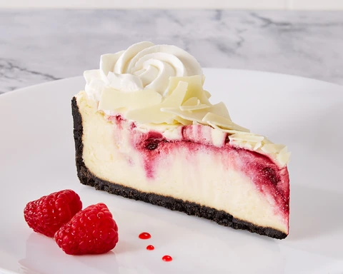Brasserie White Chocolate Raspberry Cheesecake slice with whipped cream, white chocolate, and raspberries