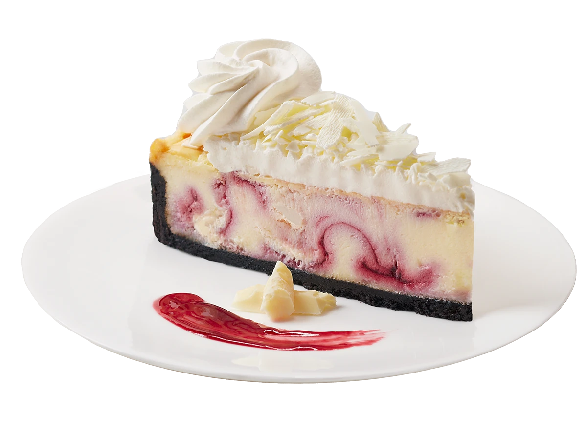White Chocolate Raspberry Cheesecake, with white chocolate shavings and raspberry sauce on a plate