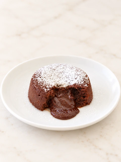 Molten lava cake opened to reveal its chocolate centre, dusted with icing sugar on a white plate
