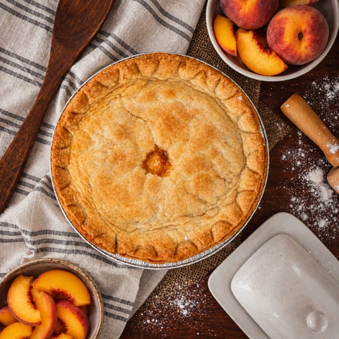 Whole peach pie photographed from above with fresh peaches